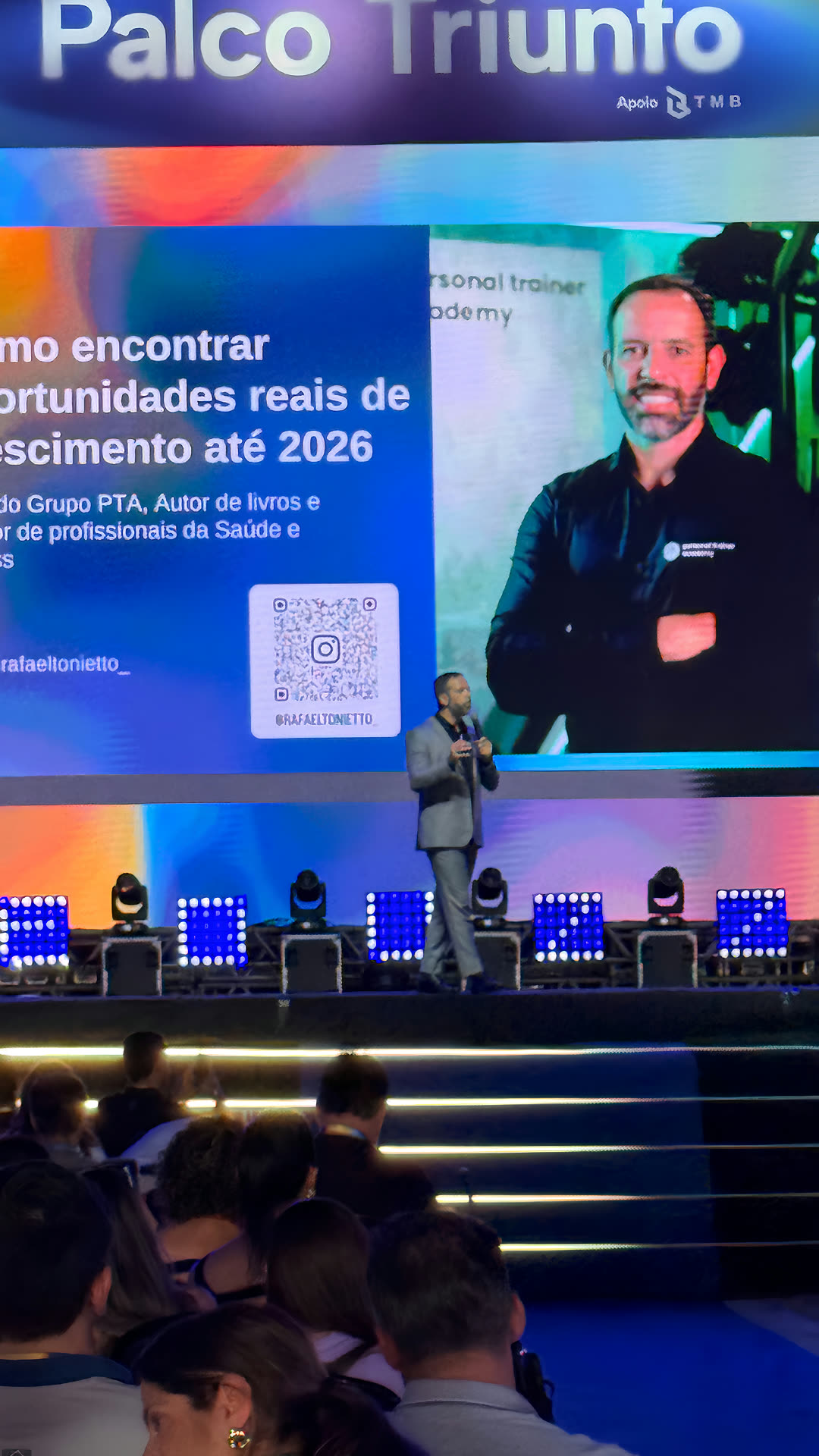 Rafael Tonietto no palco do Seven Summit, com o nome e o Instagram dele no telão e a plateia em primeiro plano