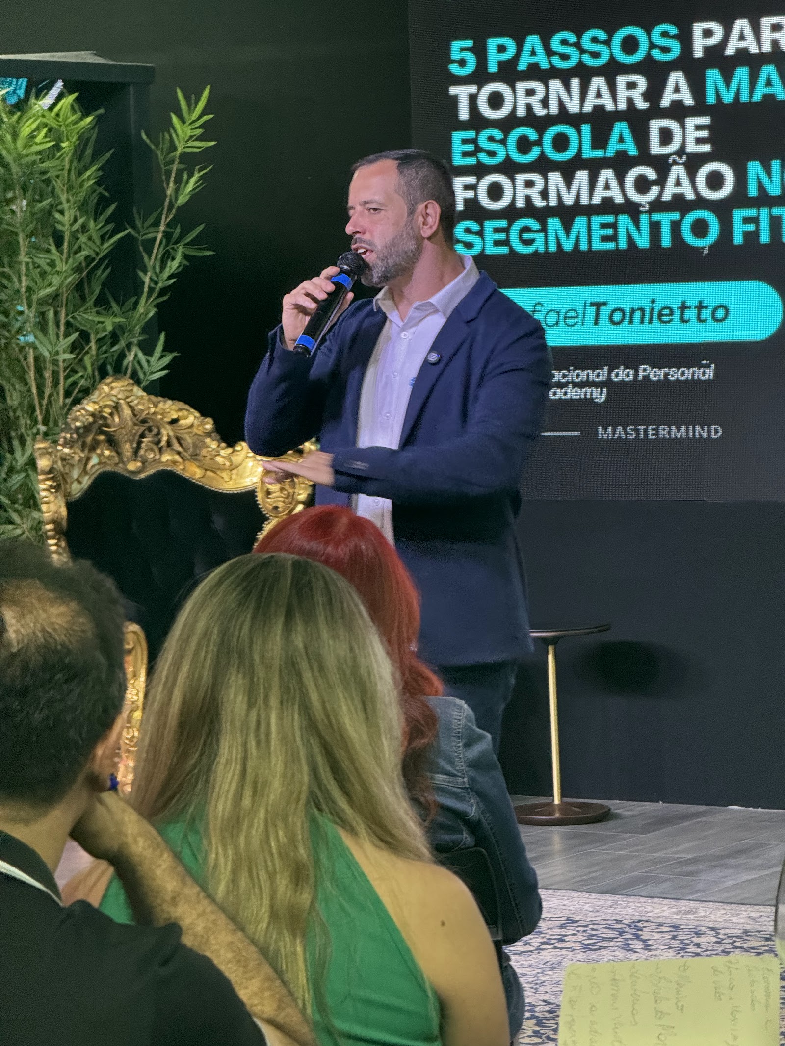 Rafael Tonietto falando ao microfone para a plateia, com o telão do Business Club Black ao fundo