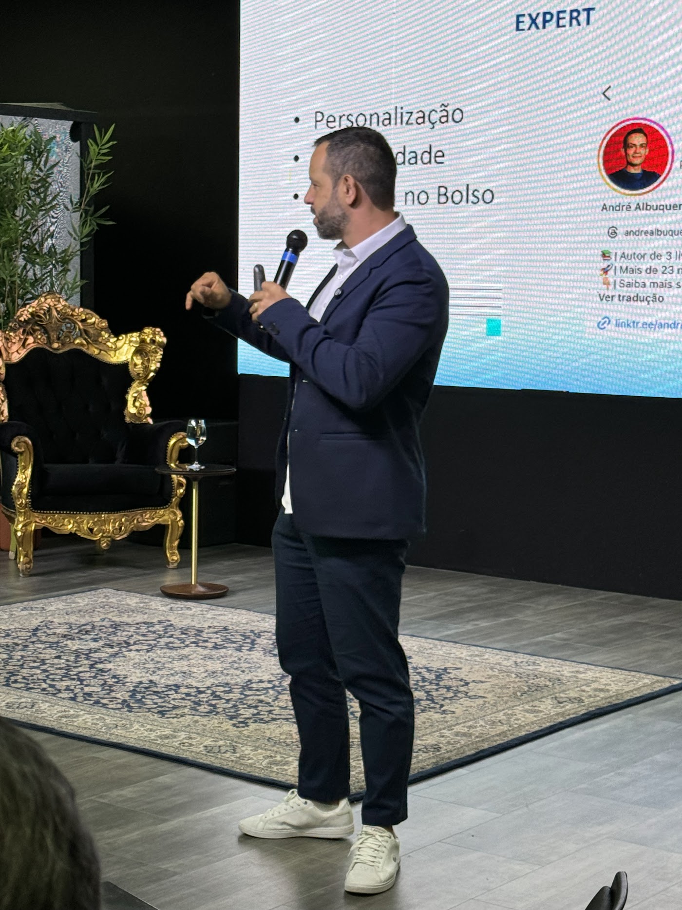 Rafael Tonietto de lado no palco, apontando para o slide enquanto fala ao microfone