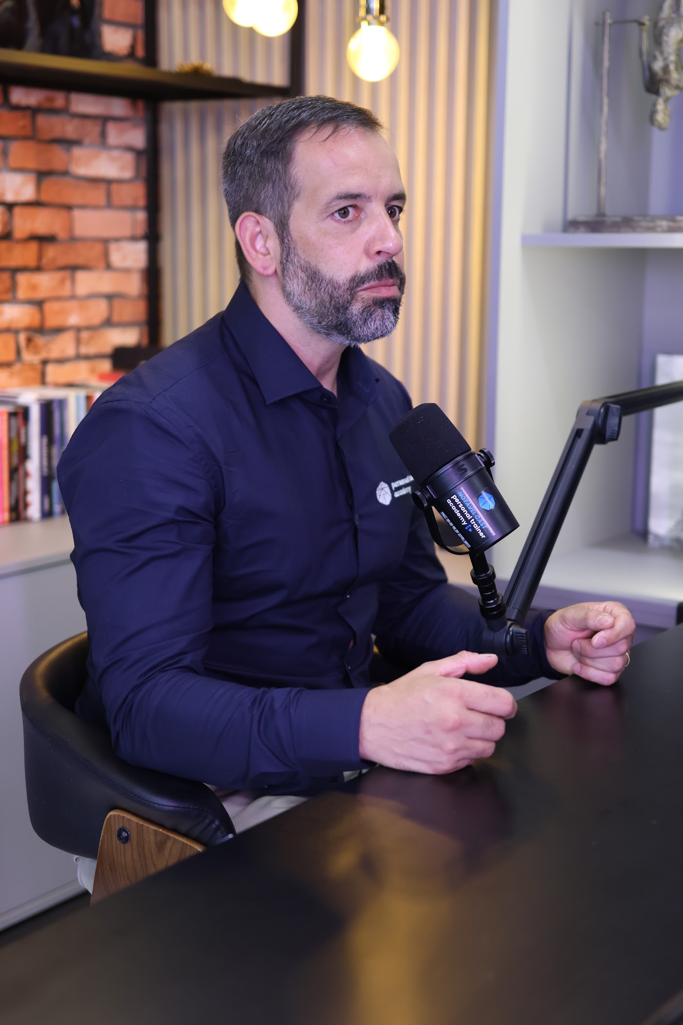 Rafael Tonietto gravando podcast, de camisa azul-marinho da Personal Trainer Academy, ao microfone